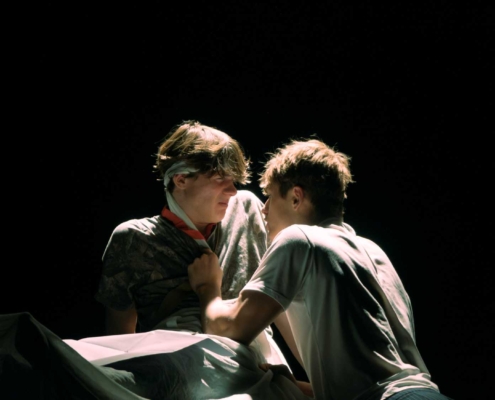 zwei Schauspieler stehen sich vor dunklem Hintergrund gegenüber