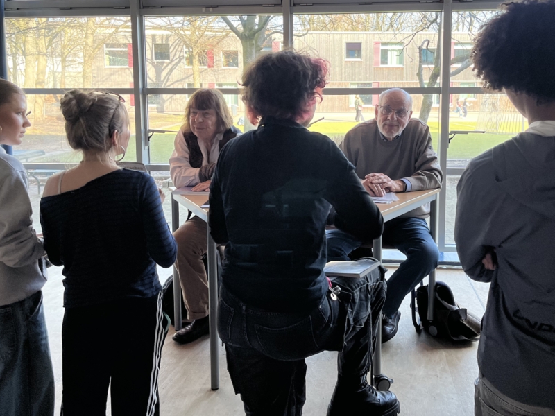 Bernhard Esser und Barbara Brix sitzen auf einer Bühne und sprechen zu Schülern des 9. Jahrgangs