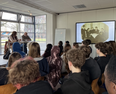 Bernhard Esser und Barbara Brix sitzen auf einer Bühne und sprechen zu Schülern des 9. Jahrgangs