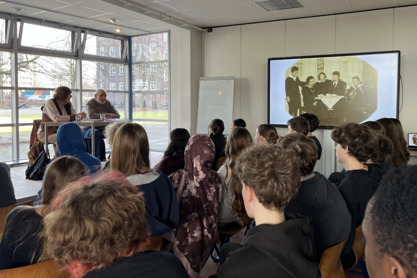 Bernhard Esser und Barbara Brix sitzen auf einer Bühne und sprechen zu Schülern des 9. Jahrgangs